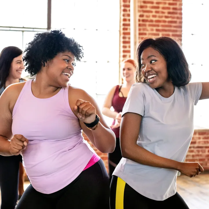Two joyful women dancing together in a lively group fitness class.