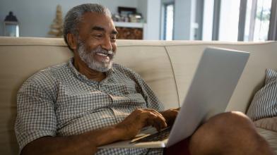 Senior African American man looking at laptop computer while sitting on couch