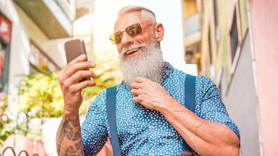 A senior man is wearing sunglasses and smiling at his phone