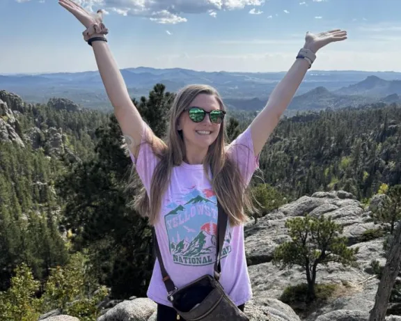A woman on a mountain top with her arms raised.