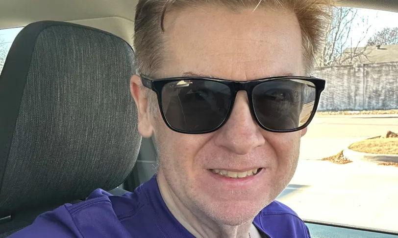 A man wearing sunglasses and a purple t-shirt.