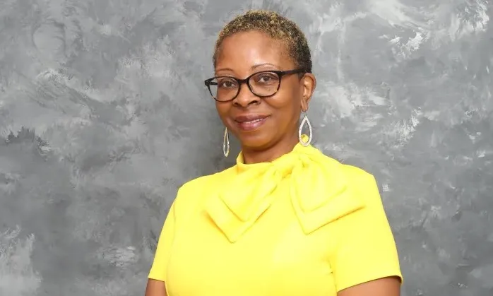 Photo of woman in yellow standing in front of gray background.