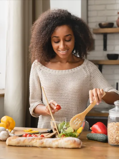 African American woman preparing salad in kitchen