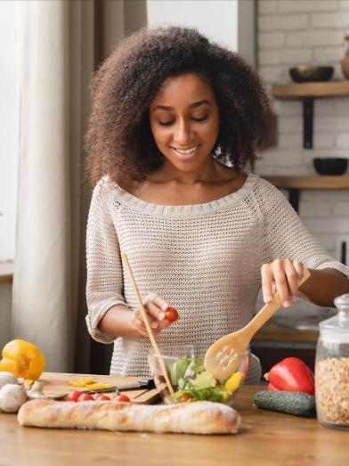 African American woman preparing salad in kitchen